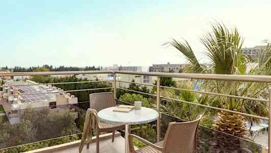 Udsigt fra en altan med bord og to stole, omgivet af træer og bygninger. (AI-genereret tekst)