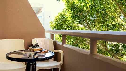 Altan med bord og stole, bøger og et par solbriller, med grønne omgivelser i baggrunden. (AI-genereret tekst)