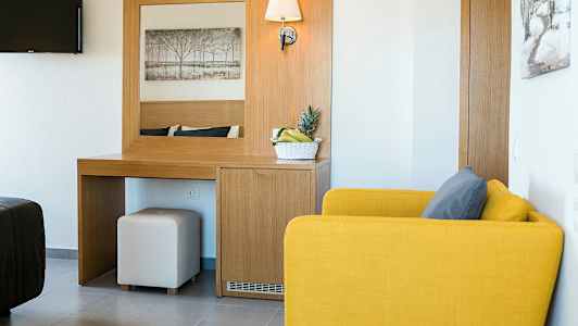 Et hotelværelse med en gul lænestol, et skrivebord med spejl og en skål med frugt. (AI-genereret tekst)