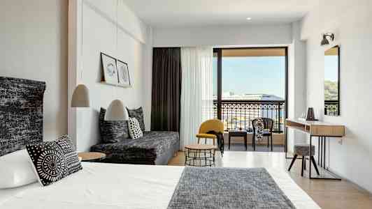 Moderne hotelværelse med seng, sofa og siddegruppe samt udsigt til balkon og omgivelser. (AI-genereret tekst)