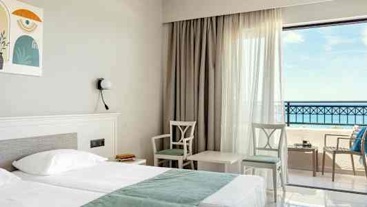 Hotelværelse med dobbeltseng, to stole og et bord ved vindue med havudsigt. (AI-genereret tekst)