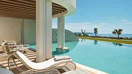 En udendørs pool med solsenge og udsigt mod havet. (AI-genereret tekst)