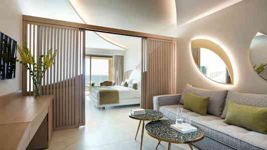 Et hotelværelse med en siddegruppe, borde og en seng i baggrunden. (AI-genereret tekst)