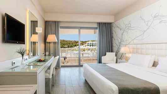 Et moderne hotelværelse med en stor seng, skrivebord, TV og altan med udsigt. (AI-genereret tekst)