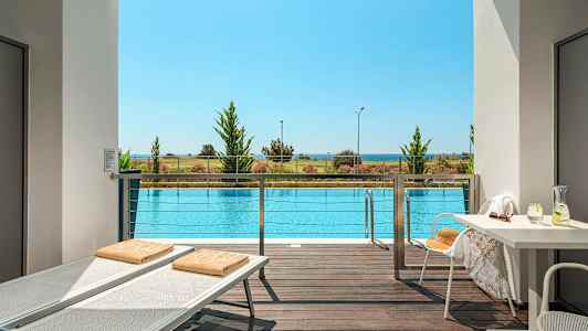 Udsigt fra terrasse over en pool med strand og hav i baggrunden. (AI-genereret tekst)