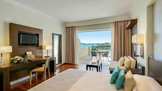 Et hotelværelse med en opredt seng, arbejdsområde, siddegruppe og åben altan med udsigt. (AI-genereret tekst)