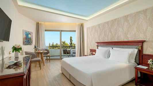 Et hotelværelse med en dobbeltseng, siddeområde og stor balkon med udsigt. (AI-genereret tekst)