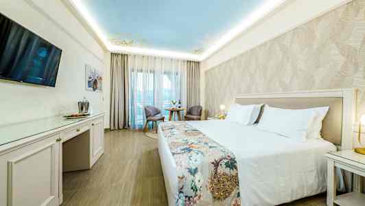 Hotelværelse med en bred dobbeltseng og et dekoreret sengetæppe, to stole og et bord ved et stort vindue. (AI-genereret tekst)