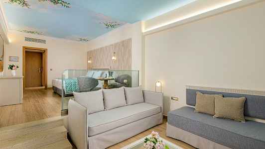 Et lyst hotelværelse med siddeområde, seng og dekoreret loft. (AI-genereret tekst)