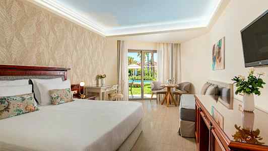 Hotelværelse med dobbeltseng, skrivebord og siddeområde. Udsigt til en have. (AI-genereret tekst)