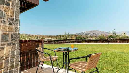 Udendørsområde med bord og to stole, græsplæne og bjerge i baggrunden. (AI-genereret tekst)