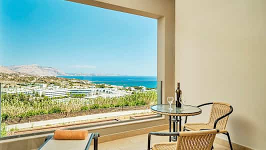 Terrasse med udsigt over havet og landskabet, bord med to stole og en liggestol. (AI-genereret tekst)