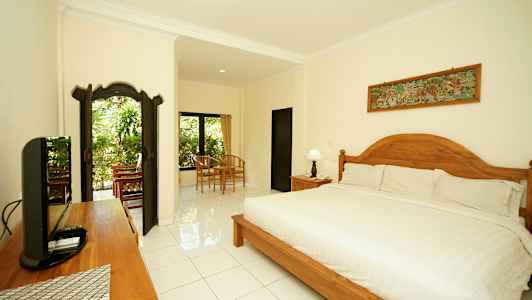 Et velindrettet og lyst soveværelse med en stor seng, træsdetaljer og siddeområde nær vinduer med udsigt til grønne omgivelser. (AI-genereret tekst)