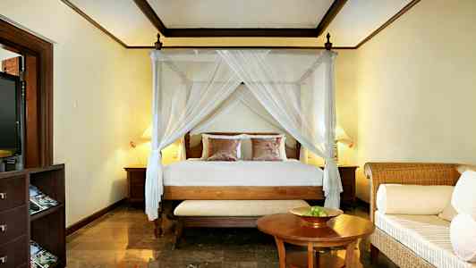 Et soveværelse med en seng med himmel, to natborde og en lille sofa foran et bord. (AI-genereret tekst)