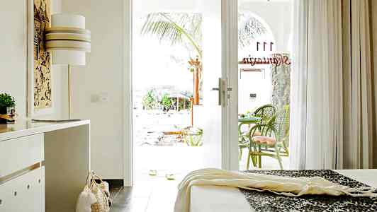 Et hotelværelse med åben glasdør til en terrasse med grønne stole. (AI-genereret tekst)