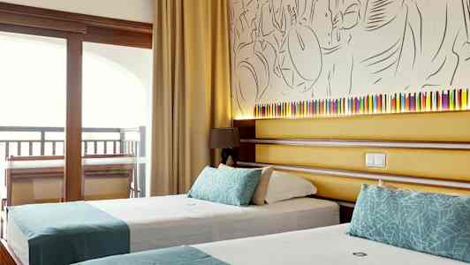 Et hotelværelse med to enkeltsenge med turkise dekorationer, bag sengene er der en væg med kunstnerisk dekoration og en lille lampe. (AI-genereret tekst)