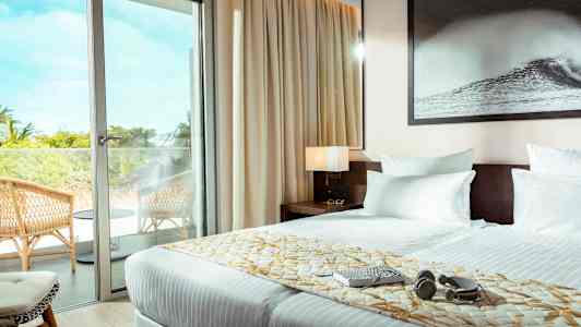 Et hotelværelse med en dobbeltseng, en glasdør der fører ud til en altan med stole. (AI-genereret tekst)