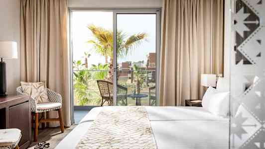 Et hotelværelse med en stor seng, et siddeområde og en balkon med udsigt til palmetræer. (AI-genereret tekst)