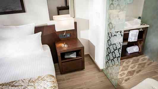 Et hotelværelse med en seng, et natbord med lamper og et badeværelse med glasdør. (AI-genereret tekst)