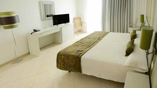 Værelse med dobbeltseng, skrivebord med spejl og TV, samt en bordlampe. (AI-genereret tekst)