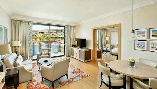 Et hotelværelse med en stue, spisebord og en altan med udsigt over en udendørs pool. (AI-genereret tekst)