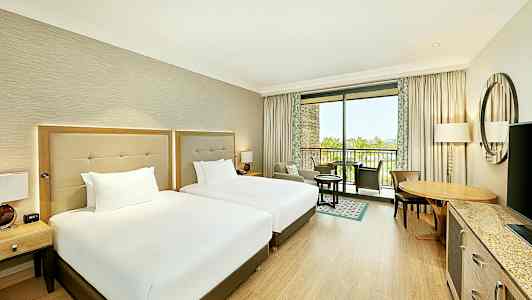 Hotelværelse med to senge og møbler samt en balkon med udsigt. (AI-genereret tekst)