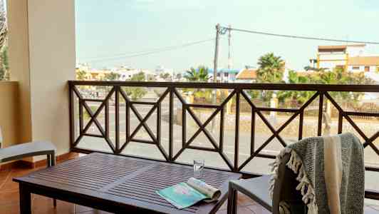 En balkon med bord og stole, med udsigt til en gade og bygninger. (AI-genereret tekst)