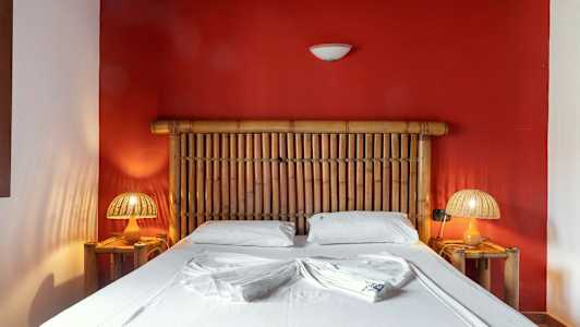 Et soveværelse med en bambusseng foran en rød væg (AI-genereret tekst)