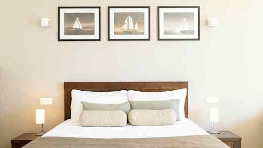 Et soveværelse med en seng, to lamper på natborde og tre billeder på væggen. (AI-genereret tekst)