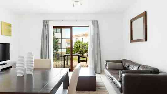 En moderne indrettet stue med spisebord, sofa og bord samt store vinduer mod en udendørsterrasse. (AI-genereret tekst)