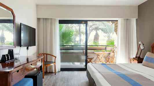 Billede af hotelværelse med seng, skrivebord og balkon med havemøbler. (AI-genereret tekst)