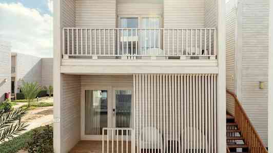 To etager med altaner i trædesign, omgivet af grønt. (AI-genereret tekst)