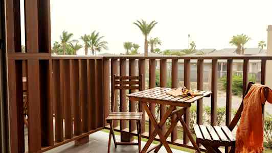 En altan med havemøbler og udsigt over palmer og andre bygninger. (AI-genereret tekst)