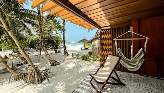 Terrasse med hængekøje og solseng, udsigt til sandstrand og palmer. (AI-genereret tekst)