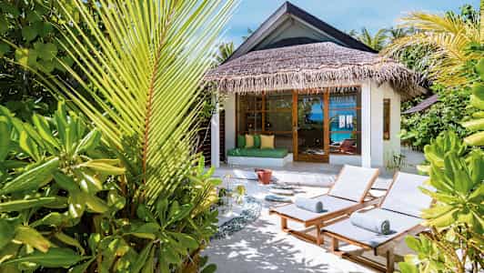 Liggestole og tropiske planter ved en bungalow med havudsigt. (AI-genereret tekst)