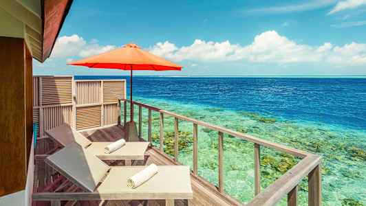 To liggestole med hvide håndklæder på en træterrasse ved havet, med en parasol. (AI-genereret tekst)