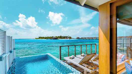 Udsigt fra en terrasse med pool og liggestole mod havet og en ø med bungalows. (AI-genereret tekst)