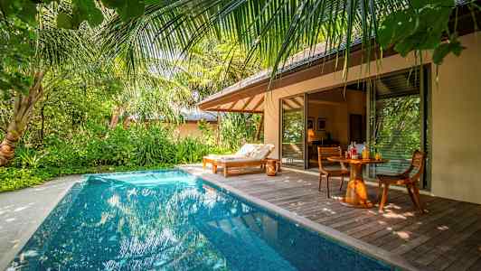 En privat pool ved en tropisk villa med en solseng og et bord med stole. (AI-genereret tekst)