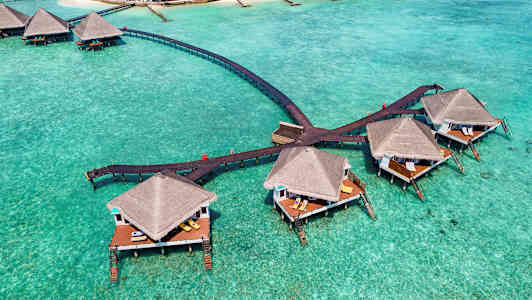 Bungalows på pæle over turkis vand, forbundet med træbroer. (AI-genereret tekst)