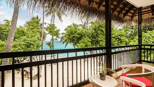 Udsigt fra en terrasse mod en sandstrand med palmer og hav. (AI-genereret tekst)