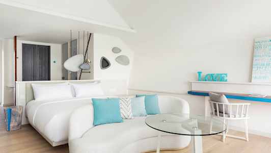 Et moderne og lyst hotelværelse med en stor seng, sofagruppe med glasbord og arbejdsområde. (AI-genereret tekst)