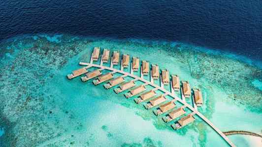 Luftudsigt over vandvillaer på en turkis lagune omgivet af hav. (AI-genereret tekst)