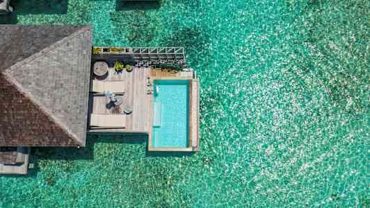 Oversigtsbillede af et solrigt vandvillaområde med en pool og klart blåt hav. (AI-genereret tekst)