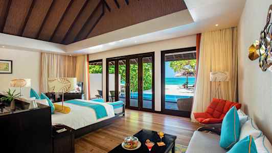 Et rummeligt værelse med seng, siddepladser og udsigt til en pool og havet gennem store vinduer. (AI-genereret tekst)