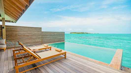 Terrasse med to solsenge ved en infinitypool og udsigt over turkisblåt hav. (AI-genereret tekst)