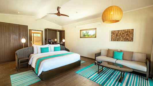 Et lyst værelse med en dobbeltseng, en sofa og et sofabord, dekoreret i turkis og neutrale farver. (AI-genereret tekst)