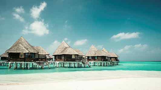 Bungalows på pæle over blåt vand ved en strand. (AI-genereret tekst)