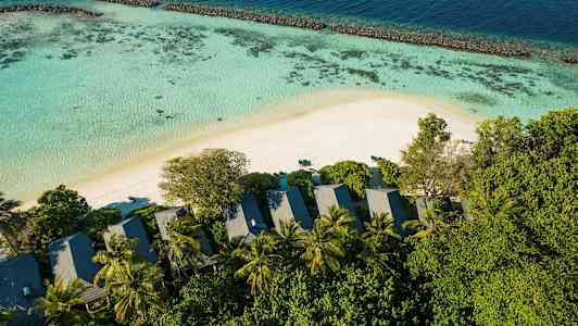 En smuk udsigt med strand, hav, koralrev og bungalower omgivet af træer. (AI-genereret tekst)