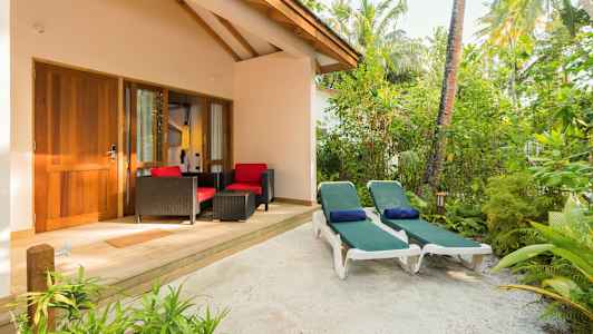 En terrasse med to liggestole og siddegruppe foran en bygning omgivet af grønt. (AI-genereret tekst)