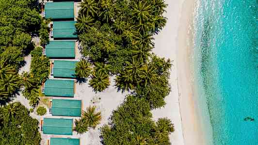 Luftfoto af frodige træer, bygninger med grønt tag og stranden ved turkis hav. (AI-genereret tekst)